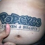 Фото татуировки на мужском животе с логотипом Popeyes Chicken & Biscuits. Простой синий рисунок.