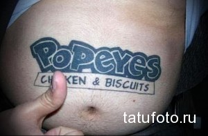 Фото татуировки на мужском животе с логотипом Popeyes Chicken & Biscuits. Простой синий рисунок.