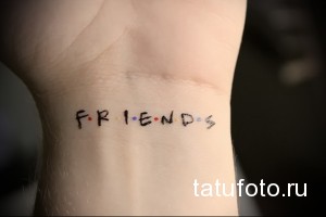 Фото тату с надписью 'Friends' на запястье, выполненной в минималистичном стиле. Черные буквы с цветными точками, напоминающими логотип сериала.
