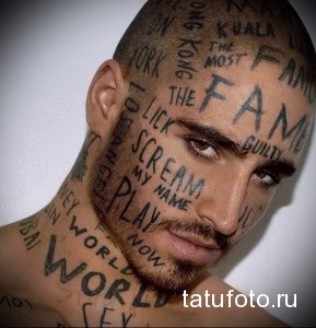 Фото тату: лицо мужчины покрыто татуировками в виде слов и фраз, выполненных черными чернилами. Экстремальный и уникальный рисунок татуировки.