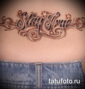 Фото тату надписи 'Stay True' на пояснице, выполненной в изящном стиле с растительными элементами и звездами.