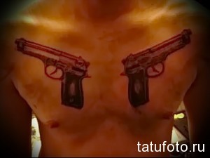 Фото тату двух пистолетов на груди. Рисунок выполнен в реалистичном стиле с использованием черных и красных оттенков.