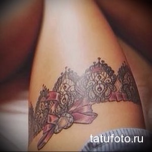 Фото тату: реалистичное изображение кружевного белья с розовым бантом на женском бедре. Детализированный рисунок татуировки выполнен в серо-розовой гамме.