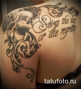 Фото тату: черно-белая татуировка черепа с розами и надписью 'Seize the day or die regretting' на плече.