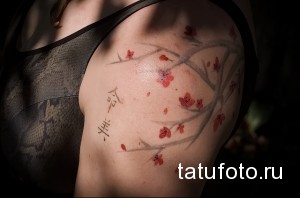Фото тату сакуры на плече в стиле акварель. Нежные розовые цветы и ветви с японской каллиграфией.