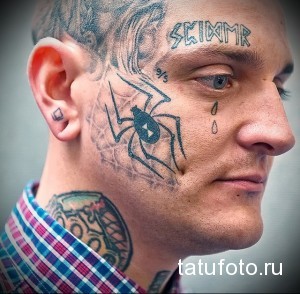 Фото тату на лице мужчины: татуировка паука на щеке, надпись на лбу и другие татуировки на лице и шее. Экстремальный стиль татуировки.