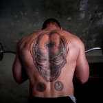 Фото тату реалистичного черепа на спине мужчины, занимающегося тяжелой атлетикой, символизирующего силу и стойкость.