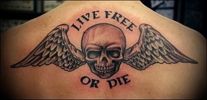 Фото тату: черно-серый рисунок черепа с крыльями и надписью "Live Free or Die" на спине. Татуировка выполнена в традиционном стиле с четкими контурами.