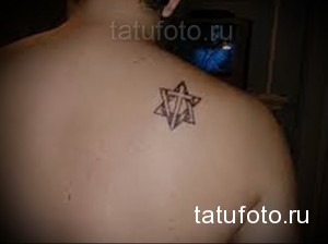 Фото небольшой татуировки Звезды Давида на лопатке. Черно-серый рисунок, выполненный тонкими линиями, символизирующий веру и идентичность.
