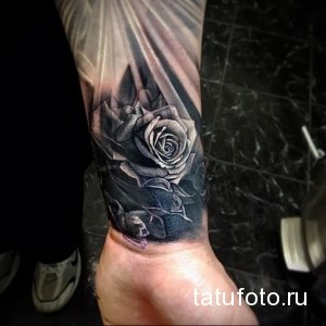 Фото тату на предплечье: Реалистичная роза с каплями росы и лучами света, выполненная в черно-серых тонах, демонстрирует мастерство тату-художника.