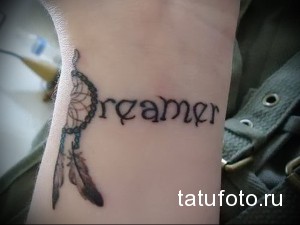 Фото тату на запястье: Ловец снов с перьями и надпись 'Dreamer' выполнены в черном цвете, создавая минималистичный и вдохновляющий дизайн.
