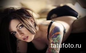 Фото тату инопланетянки с большими глазами на плече девушки. Цветной рисунок татуировки в мультяшном стиле с яркими деталями и необычным дизайном.