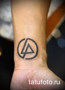 Фото тату на запястье: Черный минималистичный символ Linkin Park, состоящий из круга, треугольника и линии, выполненный в простом и лаконичном стиле.