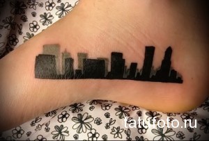 Фото тату силуэта города на стопе. Черно-белый рисунок, изображающий небоскребы и городскую архитектуру, символизирующий любовь к мегаполису.
