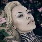 Фото тату: большая татуировка в стиле трайбл, покрывающая шею и часть груди девушки. Рисунок выполнен в черном цвете и имеет сложную геометрическую форму.