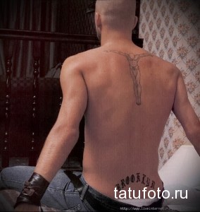 Фото тату: мужская спина украшена татуировкой с изображением распятия и надписью "BROOKLYN". Религиозный и символичный рисунок татуировки.