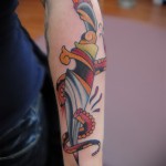 Фото тату на предплечье: традиционный кинжал с узорами, выполненный в стиле олд скул с использованием ярких цветов и четких линий.