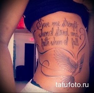 Фотография женской татуировки на боку. Надпись "Give me strength when I stand and faith when I fall" и изображение двух летящих голубей. Черно-серые тона.