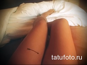 Фото минималистичной татуировки стрелы на бедре, выполненной в тонких черных линиях, с акцентом на простоту и элегантность.
