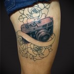 татуировка фотоаппарат и лента под надпись с цветами на ногу для девушки