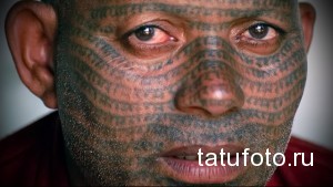 Фото мужчины с татуировкой, покрывающей все лицо. Сложный узор из геометрических фигур и линий выполнен в черном цвете.