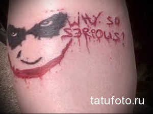 Фото тату с изображением лица Джокера и надписью 'WHY SO SERIOUS?'. Черно-красный рисунок, яркий и экспрессивный стиль, вдохновленный фильмом 'Темный рыцарь'.