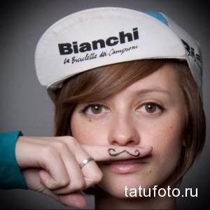 Фото тату: девушка в кепке с татуировкой усов на пальце. Классический рисунок татуировки в стиле олдскул.