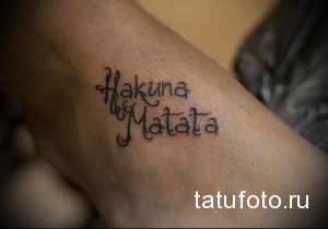 Фото тату на стопе: надпись "Hakuna Matata" выполненная простым шрифтом черными чернилами.