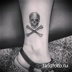 Фото тату: Череп и скрещенные кости на лодыжке. Черно-белая татуировка в традиционном стиле.
