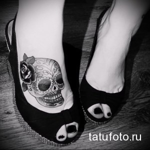Фото тату: Детализированный рисунок сахарного черепа с розой на стопе. Черно-белая татуировка в стиле чикано.