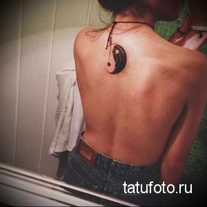 Фото татуировки на спине женщины: изображение символа Инь и Ян. Минималистичный рисунок в черно-белых тонах.