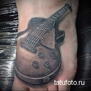 Фото тату гитары на лодыжке. Черно-белый рисунок татуировки с реалистичными деталями и тенями.