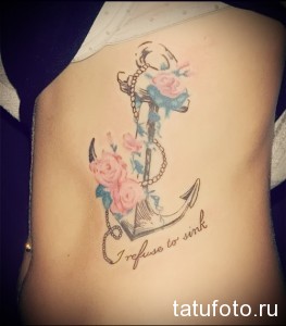 Фото тату якоря, обвитого розами, с надписью "I refuse to sink" на женском боку. Цветная татуировка в акварельном стиле.