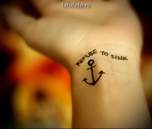 Фото тату: маленькая татуировка якоря с надписью 'REFUSE TO SINK' на запястье. Простой и мотивирующий рисунок татуировки.