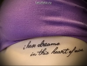Фото тату надпись на животе гласит: «I have dreams in this heart of mine». Черный рисунок татуировки выполнен каллиграфическим шрифтом.