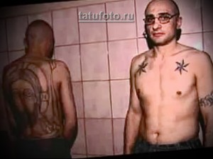 Фотография мужчины с тюремными татуировками на груди, спине и руках, включая портрет женщины и звезды. Выполнено в черно-белой гамме.