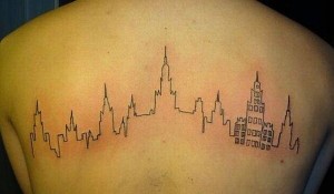 Минималистичная татуировка на спине, изображающая силуэт города, выполненный тонкой черной линией. Идеально для любителей путешествий и урбанистического стиля.