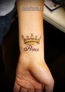 Фото татуировки на запястье с изображением золотой короны и надписи 'Prince'. Стильный и оригинальный рисунок, выполненный в ярких цветах.