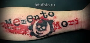 Фото минималистичной татуировки на руке с изображением черепа и надписи 'Memento Mori'. Простой и символичный рисунок татуировки.