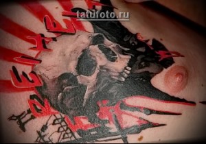 Фото тату на груди: череп с открытым ртом, окруженный красными брызгами и японскими иероглифами, выполненный в темных тонах.