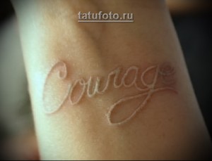 Фотография белой татуировки надписи 'Courage' на женском запястье. Минималистичный и нежный рисунок тату.