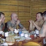 Фото тату на теле заключенных: мужчины сидят за столом, на руках и груди видны тюремные татуировки в виде звезд и надписей.