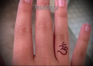 Фото тату: маленький символ "Ом" на пальце. Простой и духовный рисунок татуировки.