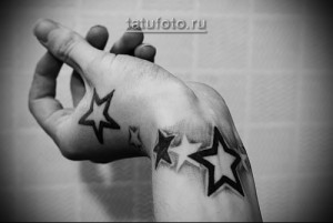 Черно-белое фото татуировки с изображением нескольких звезд разного размера на запястье. Простой и стильный рисунок.