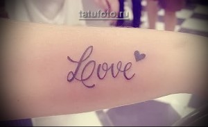 Фото тату: надпись "Love" красивым шрифтом с маленьким сердечком на запястье. Нежный и романтичный рисунок татуировки для девушек.
