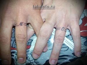 Фото парных татуировок с инициалами "M" и "C" в виде браслетов на пальцах. Минималистичный дизайн, черные чернила.