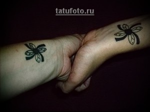 Фото парной татуировки на запястьях: два стилизованных четырехлистных клевера в черном цвете.