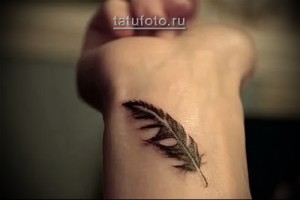 Фото татуировки в виде пера на запястье. Рисунок выполнен в коричневых тонах с детальной проработкой текстуры пера.