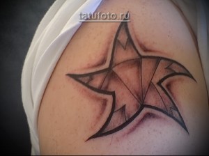 Фото татуировки на плече мужчины: звезда, разбитая на осколки, с темным контуром и светлой заливкой. Рисунок выполнен в реалистичном стиле.