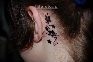 Фото татуировки на затылке с изображением нескольких маленьких черных звезд и завитков. Минималистичный и аккуратный рисунок.